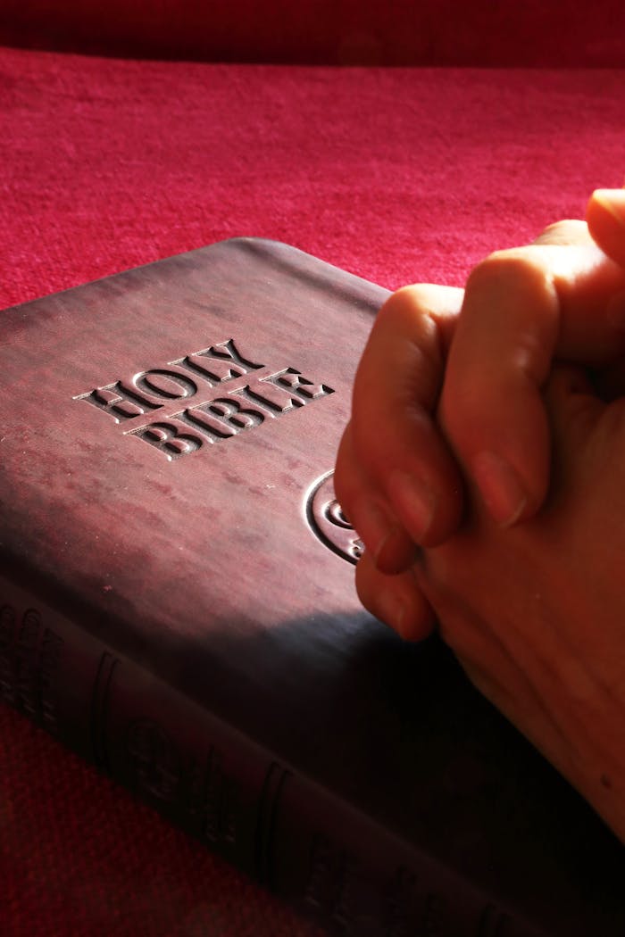 services-03 Close-up of hands praying on a Holy Bible, symbolizing faith and spirituality.